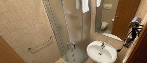 A bathroom with a glass shower enclosure, a sink, a toilet, and a hairdryer mounted on the wall.