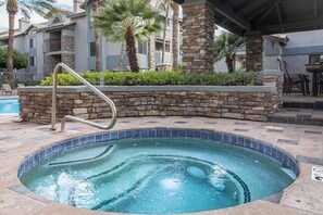 A hot tub with a stone wall and metal handrail, surrounded by a pool area with palm trees and a building in the background. - Resort Style Biltmore Condo (Phoenix)