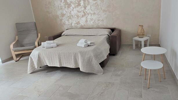 A bedroom with a bed, a chair, two small tables, and a textured wall.