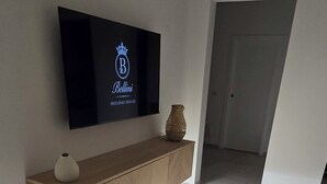 A modern interior with a flat-screen TV mounted on a wall, a wooden console table with decorative items, and a tiled floor.