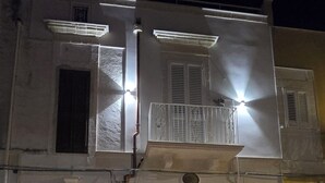 A two-story building with a white facade, a balcony, and a parked car in front.