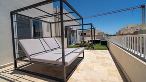 A balcony with a glass enclosure, a cushioned seating area, and a view of a construction site in the background.