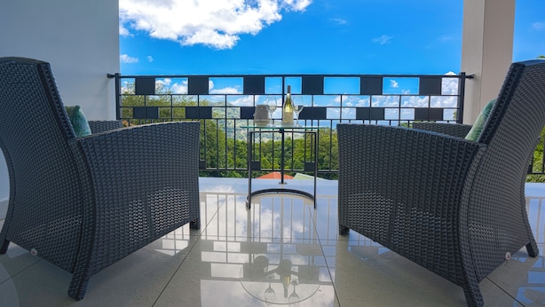 Un balcon doté de meubles en osier et offrant une vue dégagée sur le ciel et la verdure.