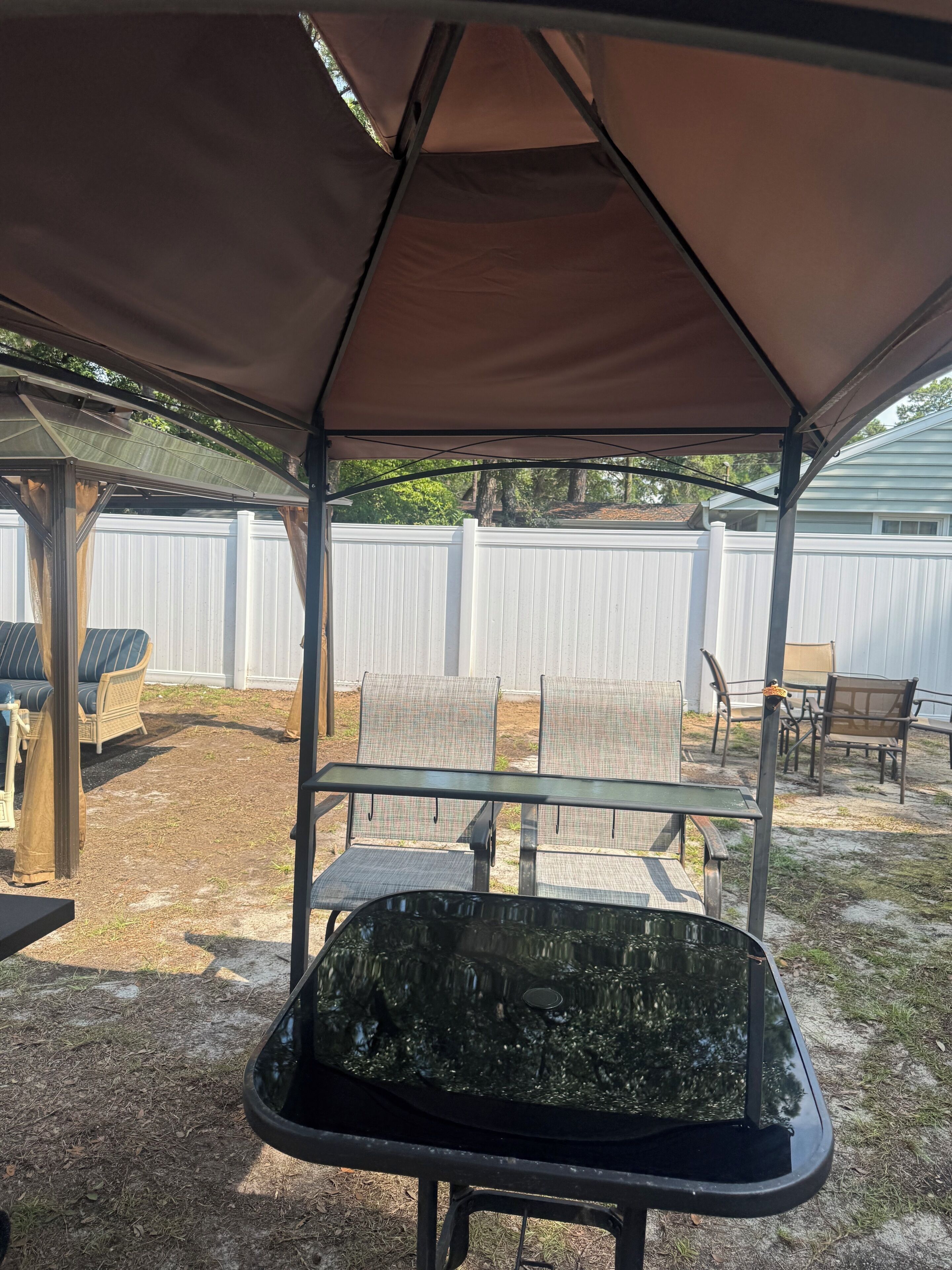 Un patio couvert avec une table et des chaises, une clôture blanche en arrière-plan et une terrasse en bois.