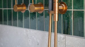 Un baño con pared de azulejos verdes y ducha con grifo y manguera dorados.