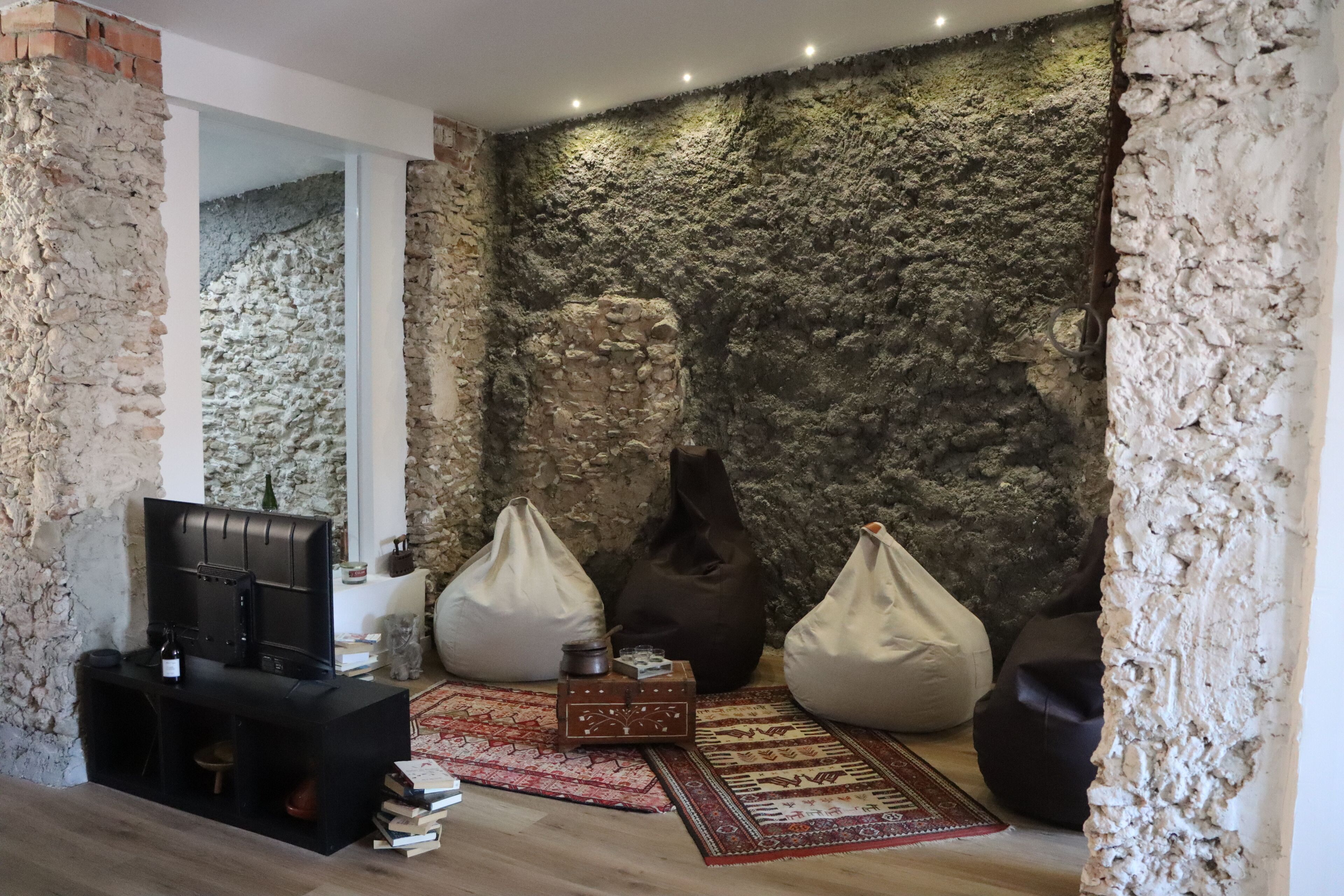 Una sala de estar con pared de piedra, televisor, pufs y una mesa de centro.