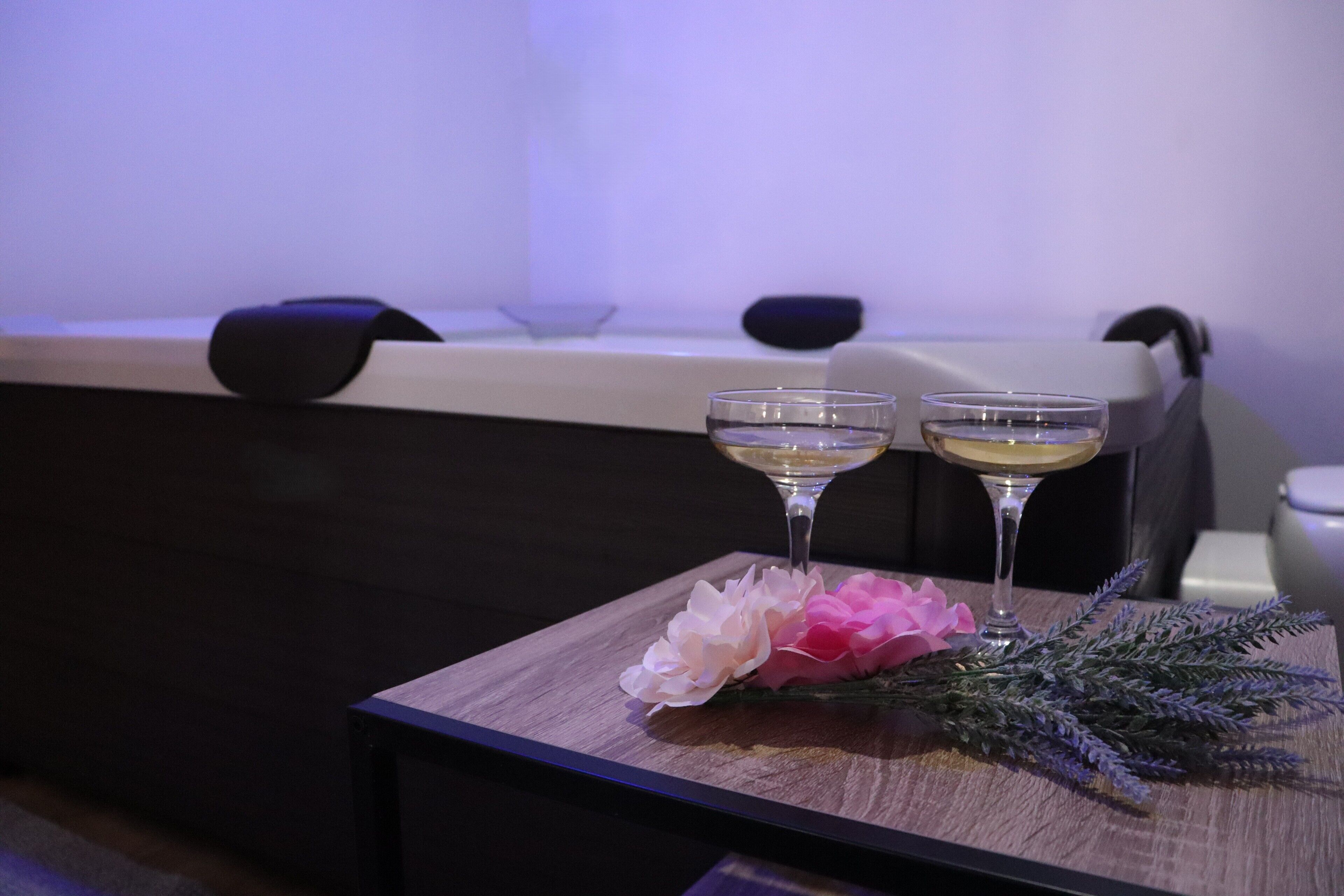 A table with two glasses of a clear beverage, a pink flower, and a sprig of greenery.