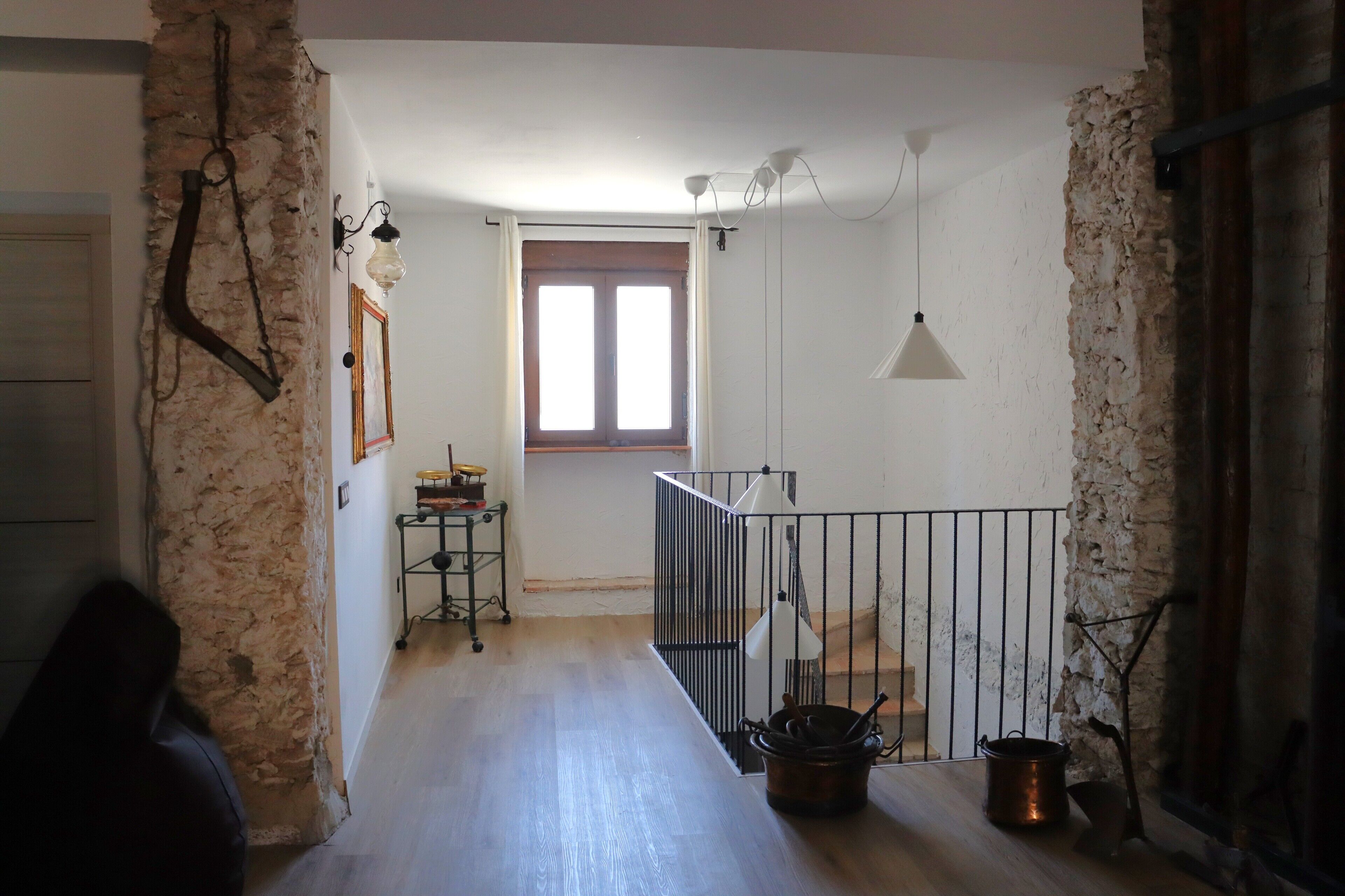 Un pasillo estrecho con suelo de madera, barandilla de metal y una ventana con cortinas.