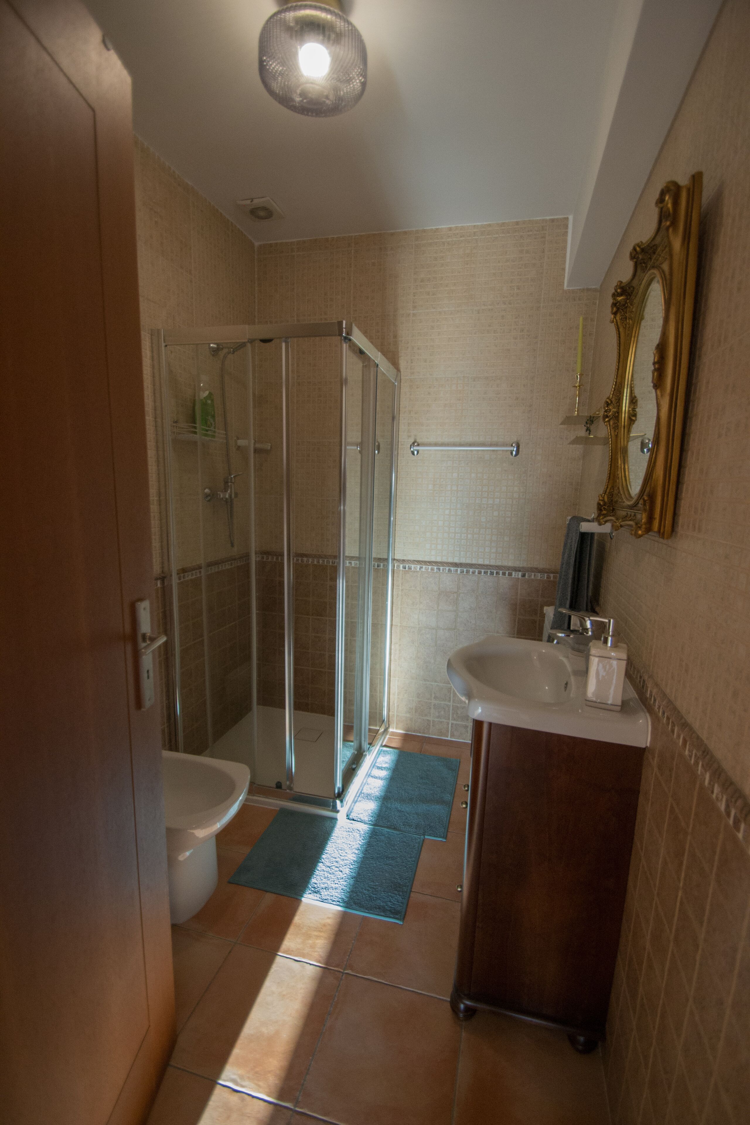 A bathroom with a glass shower enclosure, a toilet, a sink, and a mirror.