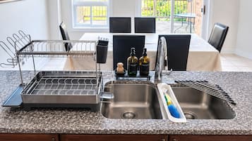 Une cuisine dotée d’un plan de travail en granit, d’un évier en acier inoxydable, d’un égouttoir et d’une fenêtre donnant sur un balcon.