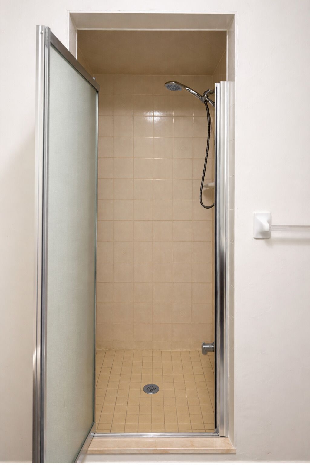 Una ducha a ras de suelo con puerta de cristal, paredes de azulejos color beige y un cabezal de ducha.