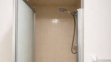 Una ducha a ras de suelo con puerta de cristal, paredes de azulejos color beige y un cabezal de ducha.