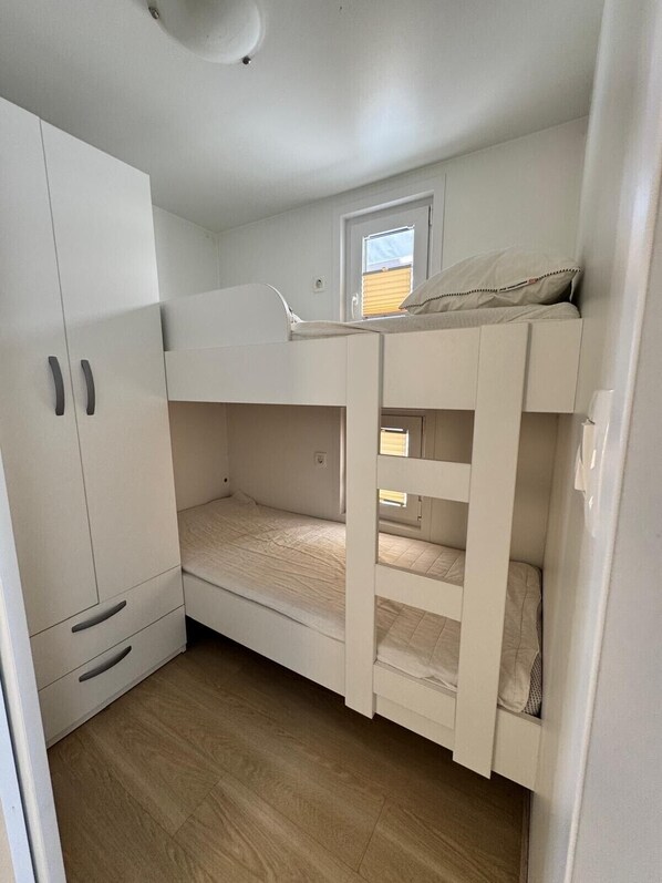 A compact room with a bunk bed, a wardrobe, and a small window.