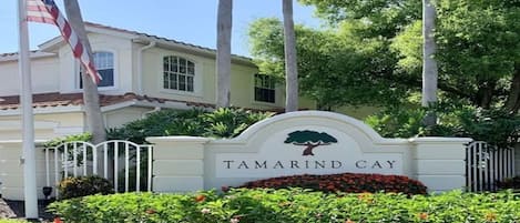 Uma entrada com portão e placa indicando "Tamarind Cay", além de um mastro com a bandeira americana.