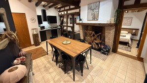 A cozy dining area with a wooden table and chairs, a fireplace with a decorative log, and a kitchen in the background. - Charming Solognese house for 4 people (Pierrefitte-sur-Sauldre)