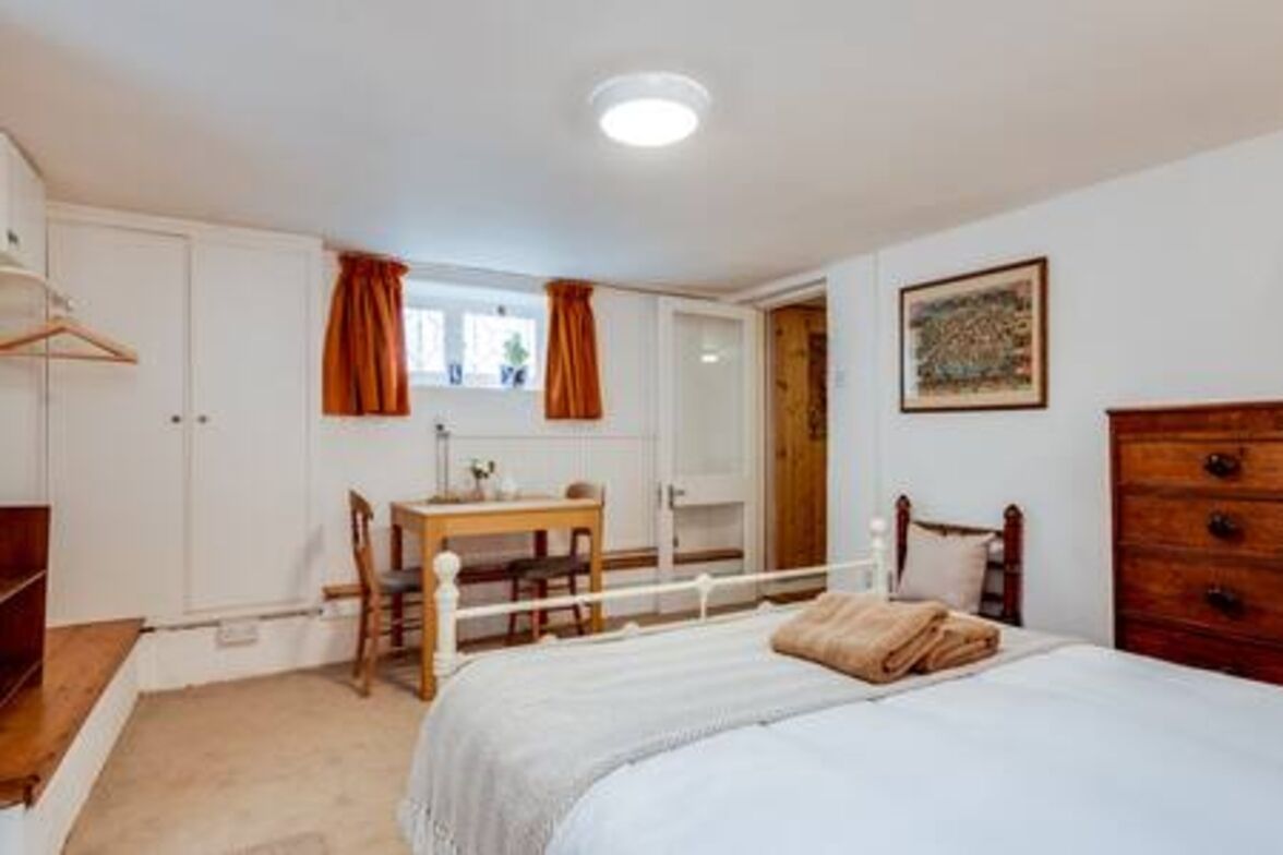 A bedroom with a bed, a wooden dresser, a desk with a chair, and a window with curtains.