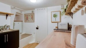 Une cuisine avec un plan de travail en bois, un réfrigérateur blanc et une étagère murale où sont rangés de la vaisselle.