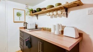 Une cuisine avec un plan de travail en bois, une machine à café, un grille-pain et une étagère où sont rangés de la vaisselle et un tableau encadré.