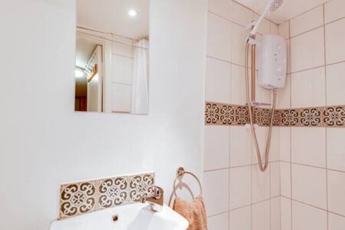 A bathroom with a white sink, a towel rack, and a shower with a control panel.