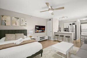 Una habitación de hotel moderna con una cama grande, un escritorio, un televisor y una kitchenette.