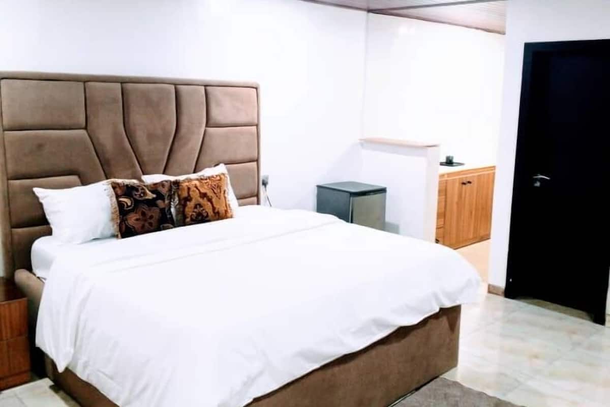 A modern bedroom with a tufted headboard, a large bed with white bedding, and a small bedside table.