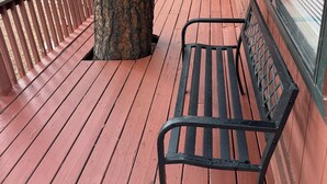 Una terraza de madera con un banco, un árbol y un edificio con ventanas grandes.