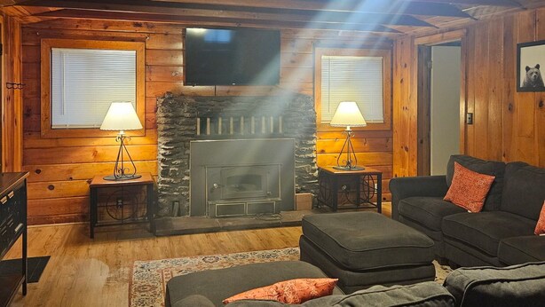 Un interior acogedor de cabaña de madera con chimenea, dos lámparas, un televisor y un sofá.