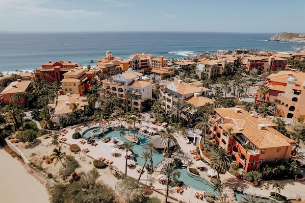 A resort with multiple buildings, a central pool, and a view of the ocean.
