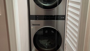 Máquina de lavar e secar roupa compacta, com frente de aço inoxidável, instalada em um corredor estreito.