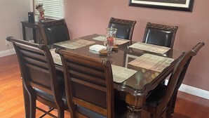 Uma sala de jantar com uma mesa e cadeiras de madeira, um vaso e um quadro na parede.
