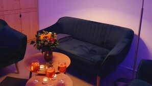 A cozy living room with a dark blue sofa, a round wooden coffee table with drinks and candles, and a floor lamp. - Oderbruch26 Your vacation home with sauna option (Letschin)