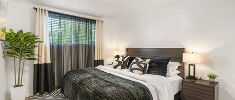A modern bedroom with a large bed, dark headboard, two bedside tables with lamps, and a zebra-patterned rug.