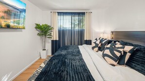 Ett modernt sovrum med en stor säng, en krukväxt och en tavla på väggen.