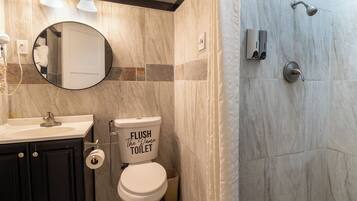 A bathroom with a toilet, sink, mirror, and shower.
