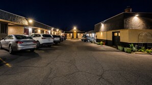 Un estacionamiento con varios coches aparcados frente a un edificio de múltiples puertas y ventanas, lo que sugiere un hotel u otro establecimiento similar.