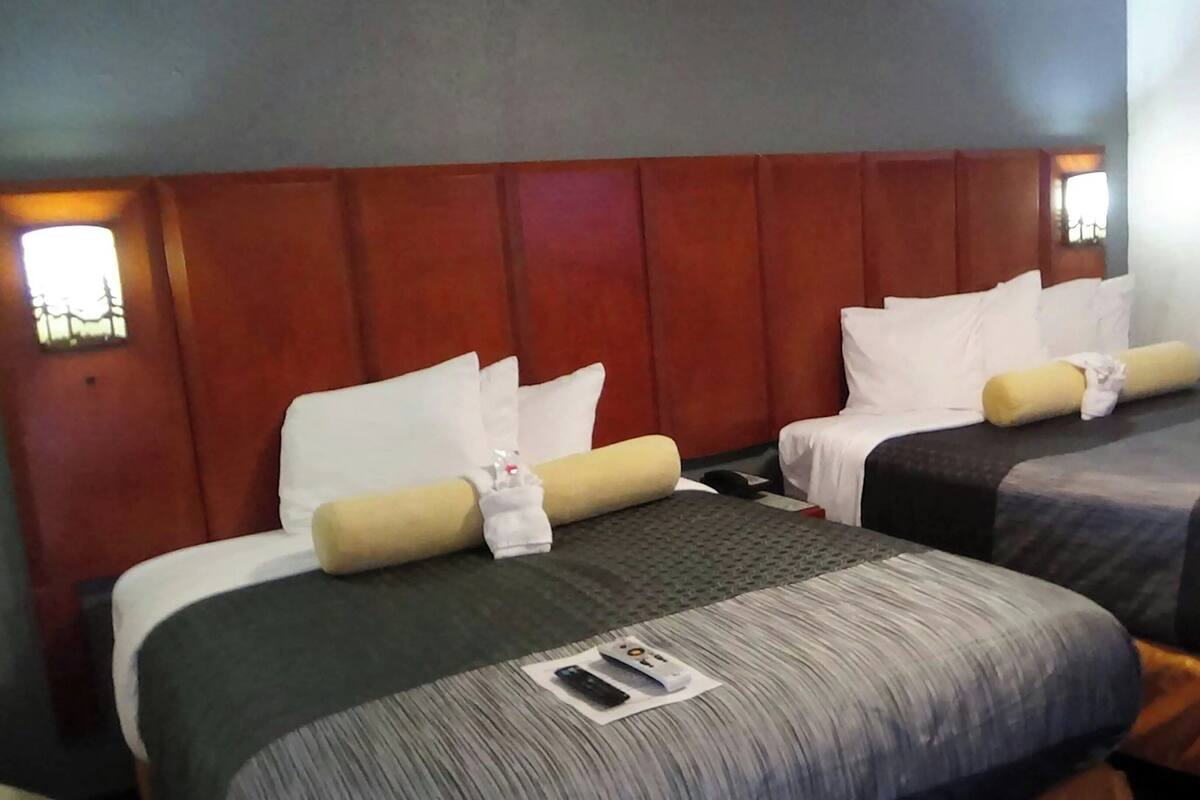 Une chambre d’hôtel avec deux lits, chacun étant équipé d’un oreiller et d’une couverture. Une télécommande se trouve sur le sol, entre les deux lits.