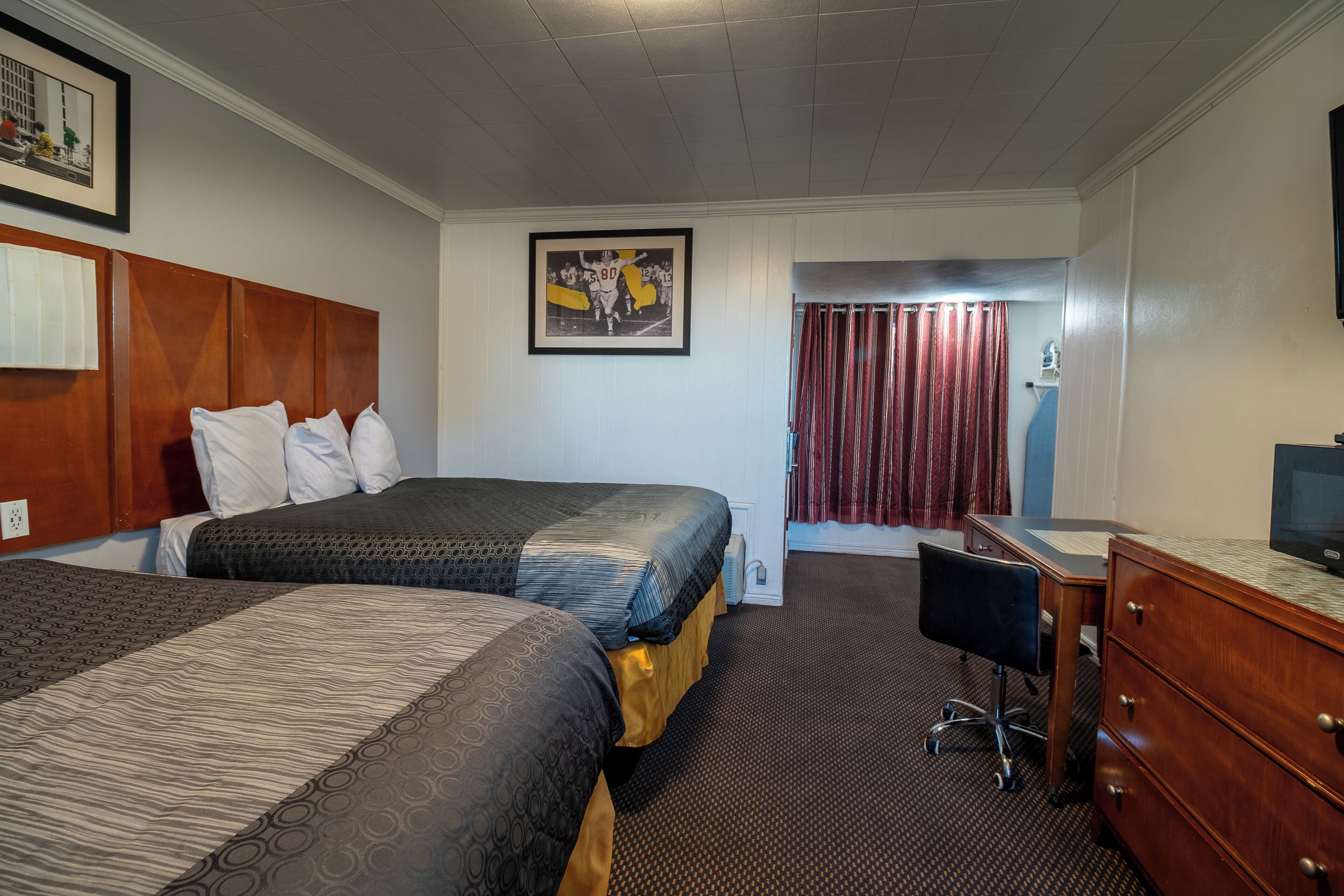 Habitación de hotel con dos camas, un escritorio, una silla, un televisor y un cuadro en la pared.