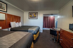 Habitación de hotel con dos camas, un escritorio, una silla, un televisor y un cuadro en la pared.