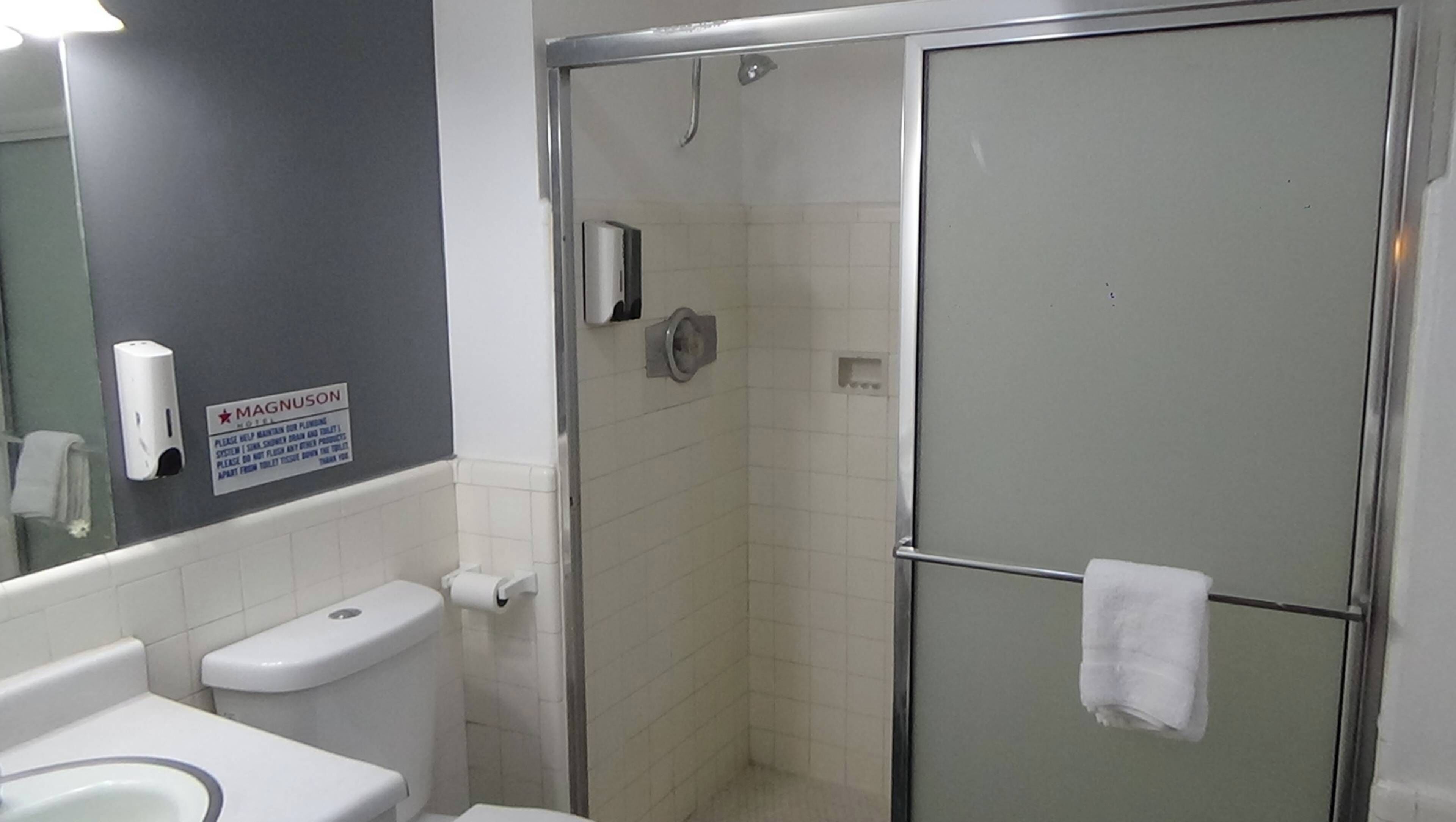 Baño con inodoro, secamanos, cabina de ducha y barra para toallas.
