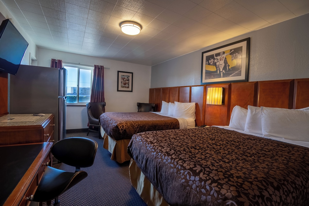 A hotel room with two beds, a desk, a chair, a television, and a window with curtains.