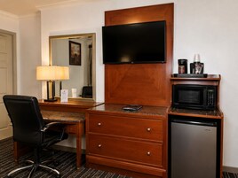 A hotel room with a desk, chair, television, microwave, and refrigerator.