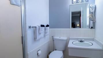Un baño con inodoro, lavamanos, toallero y un espejo con luces arriba.
