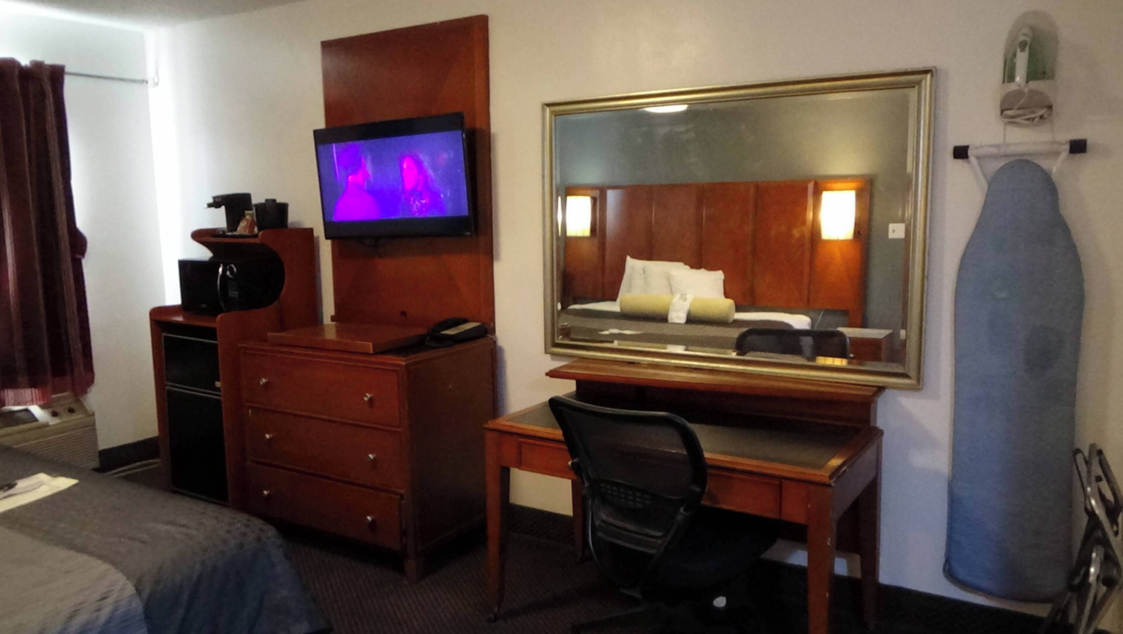 A hotel room with a bed, a desk with a chair, a television, a dresser, and a mirror.