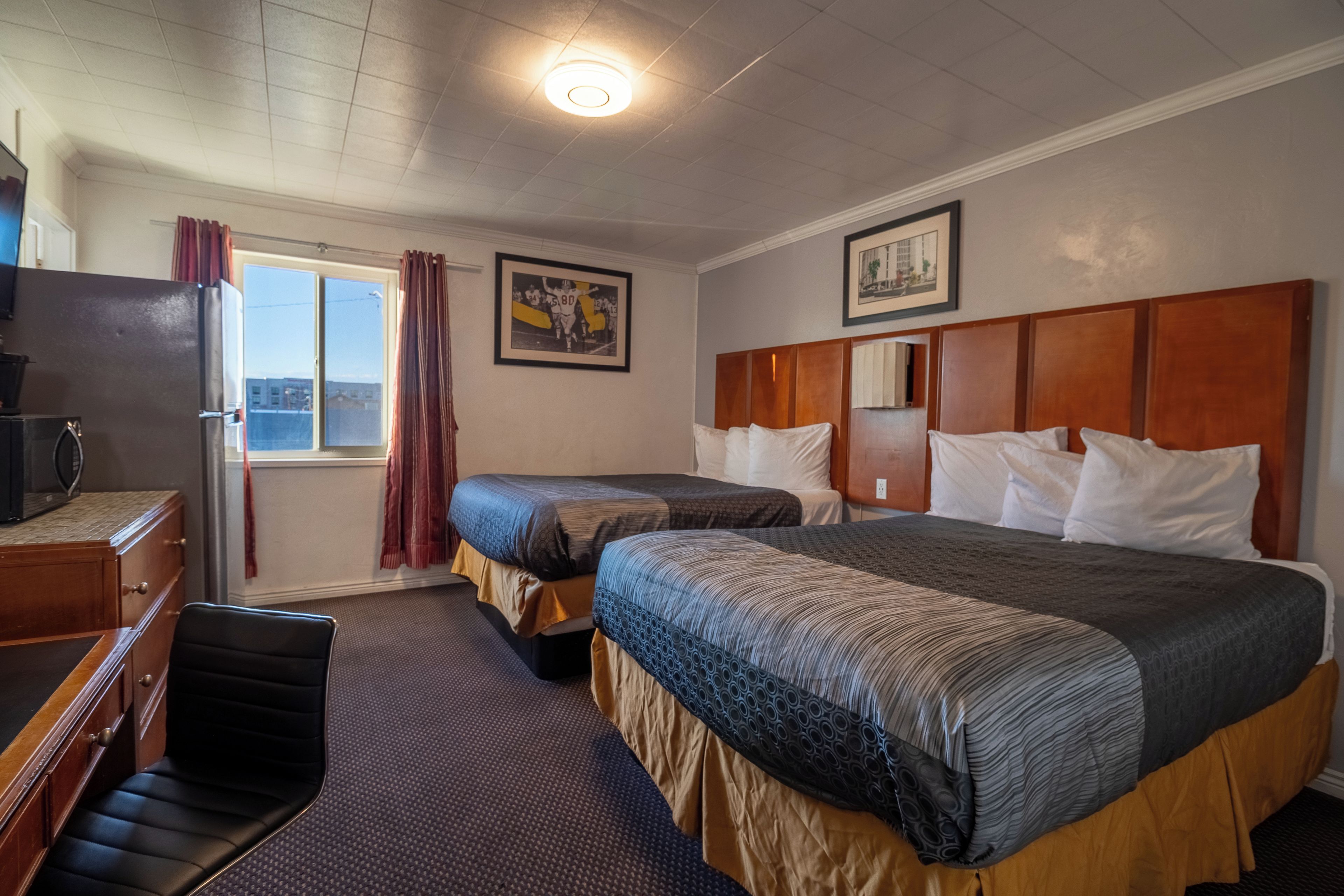 Een hotelkamer met twee bedden, een bureau, een stoel, een televisie en een raam met gordijnen.
