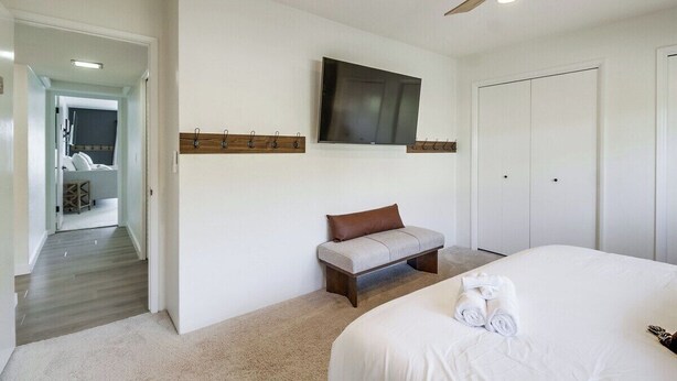 Une chambre d’hôtel avec un lit, un téléviseur fixé au mur, un banc et une porte.