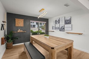 A modern dining area with a wooden table and bench, a black wall with a wooden cabinet, and framed cityscape pictures on the wall.