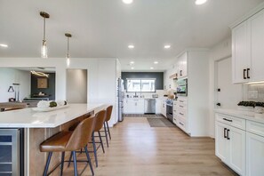 Une cuisine moderne avec des meubles blancs, un îlot central doté de tabourets et un éclairage suspendu.