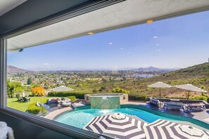 Une piscine entourée de chaises longues et de parasols, elle-même bordée d’un jardin aménagé et offrant une vue sur une vallée.