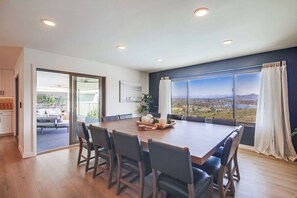 A spacious dining area with a large table and chairs, a view of the outdoors through a large window, and a sliding glass door leading to an outdoor seating area.