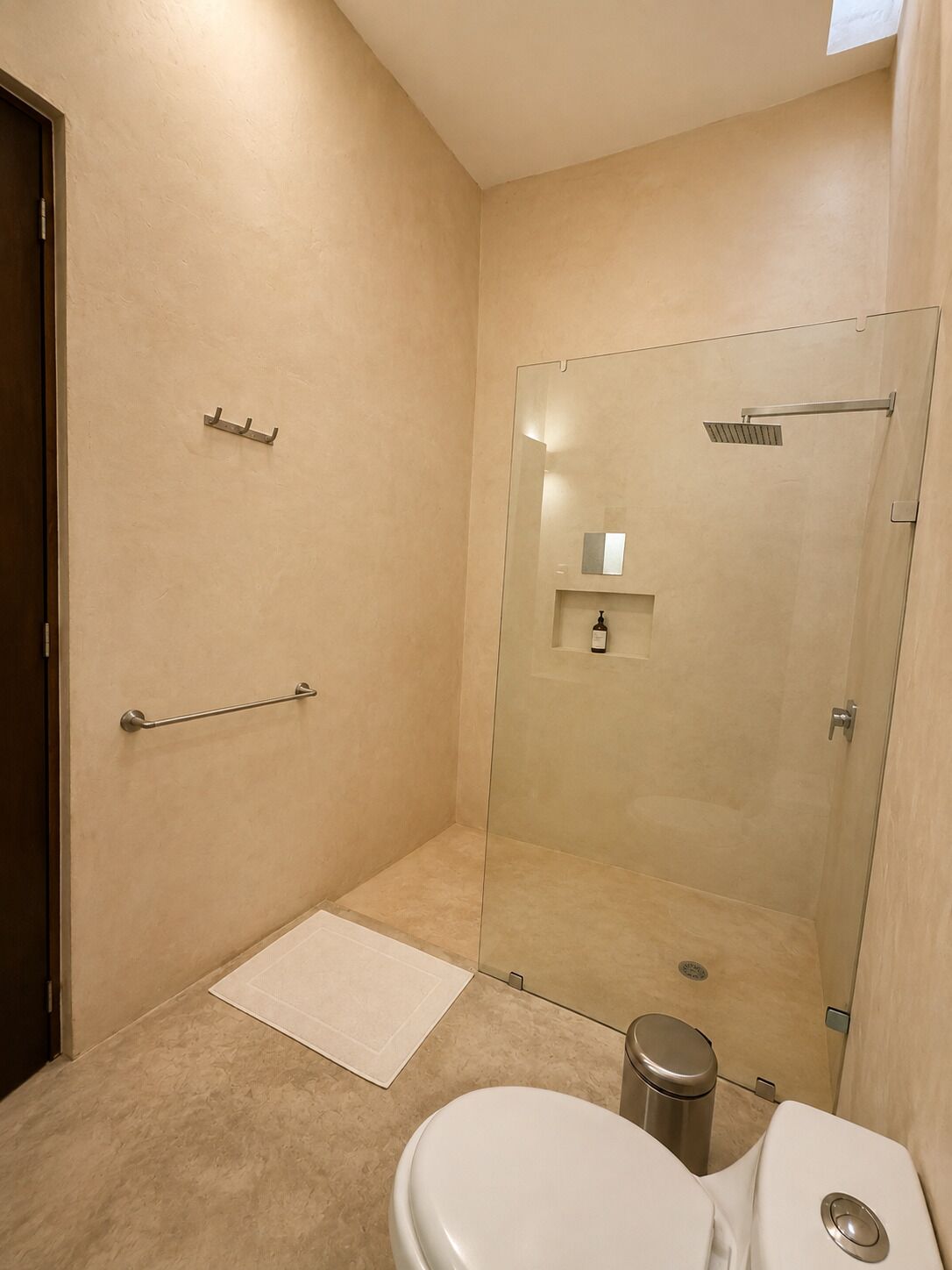 A bathroom with a glass shower enclosure, a toilet, and a small trash bin.